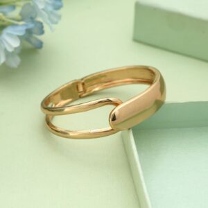 Gold-toned hinged cuff bracelet featuring an asymmetrical split-band design with a solid polished overlapping cap, resting on a soft green surface.