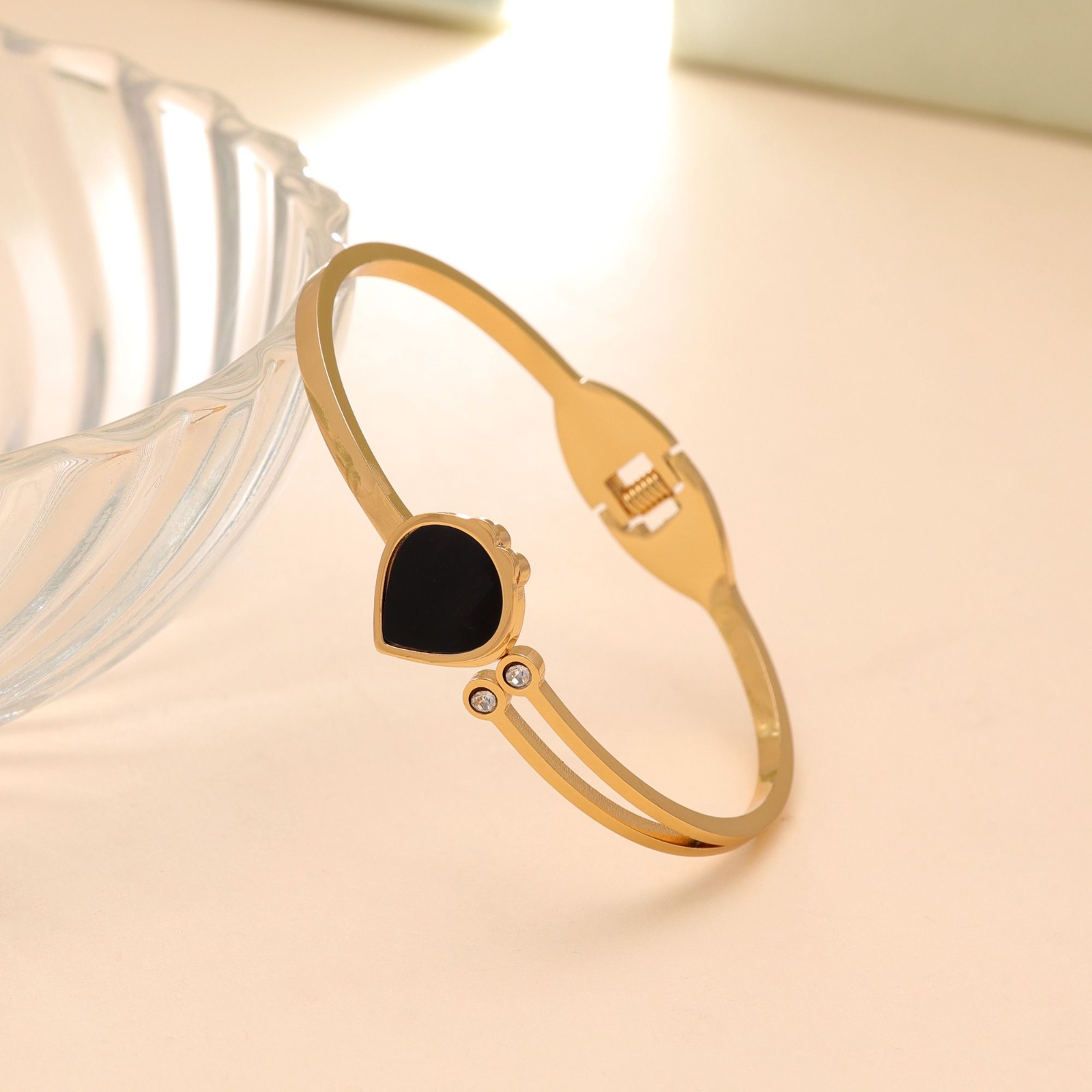 Gold bangle bracelet with a black teardrop enamel centerpiece and two small round crystal accents.
