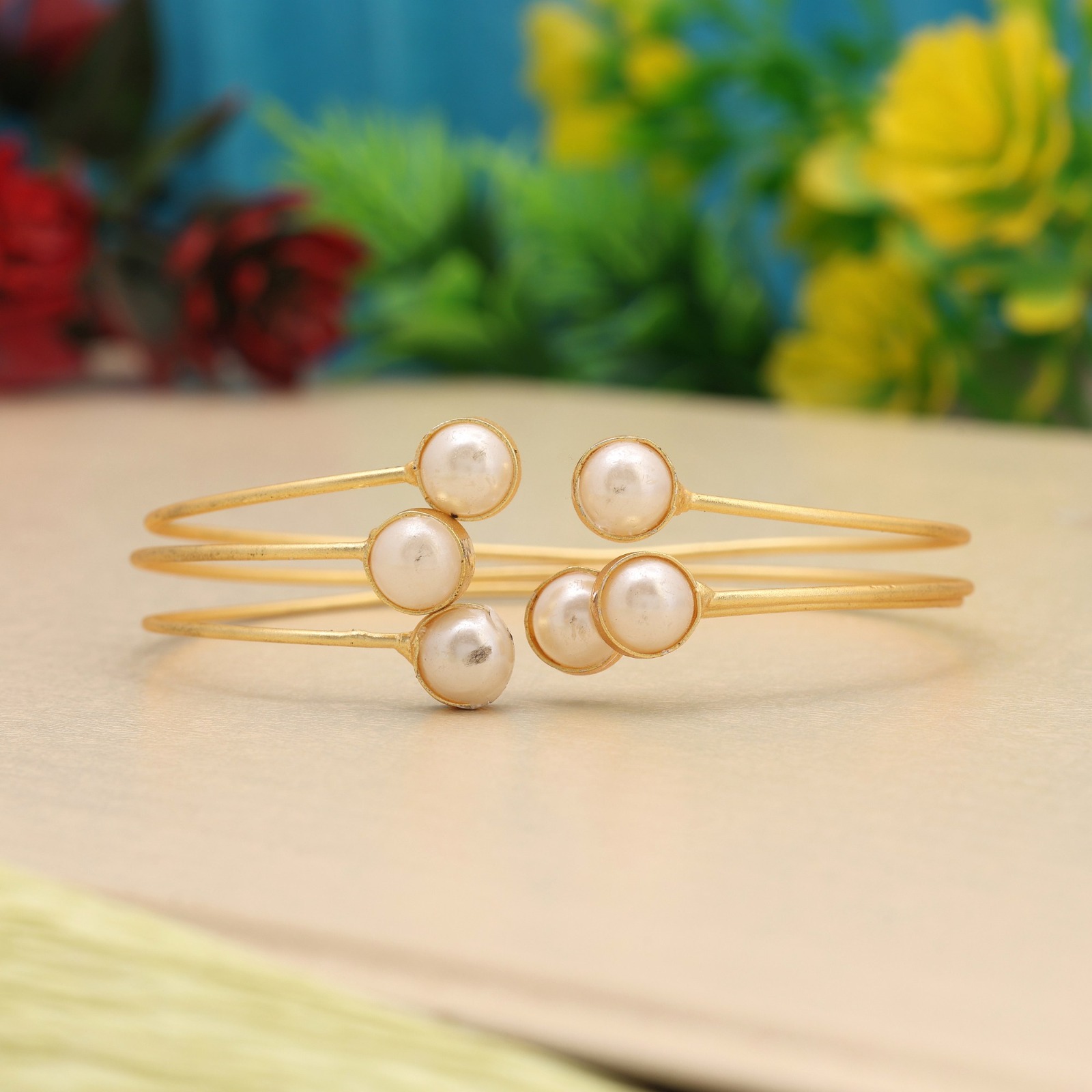 Matte gold-toned triple wire open cuff bracelet featuring bezel-set white faux pearls on each open end, displayed on a gray surface.