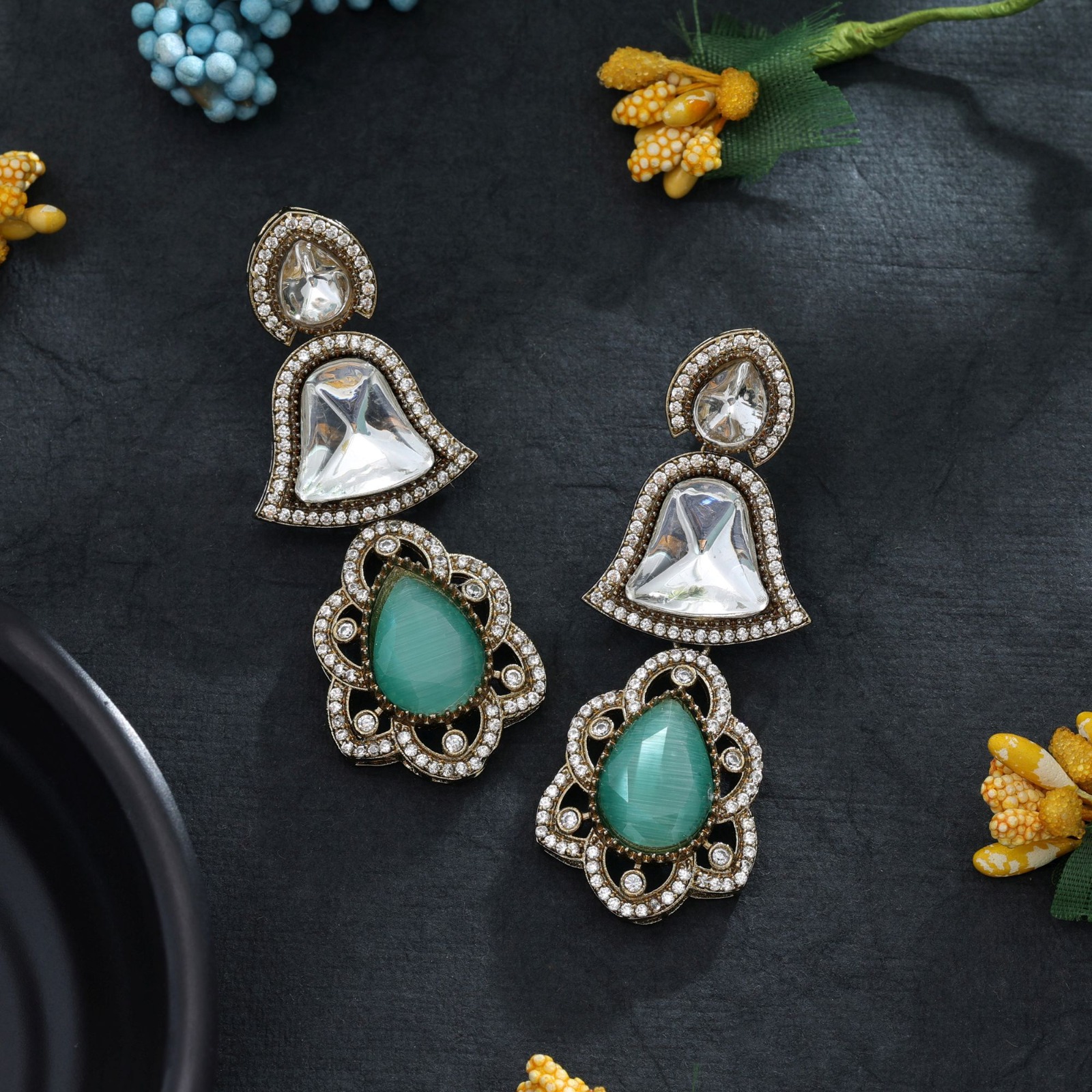 Statement drop earrings featuring bell-shaped clear accents, deep sapphire-blue Monalisa stone teardrop pendants, and a micro-pave American Diamond halo.