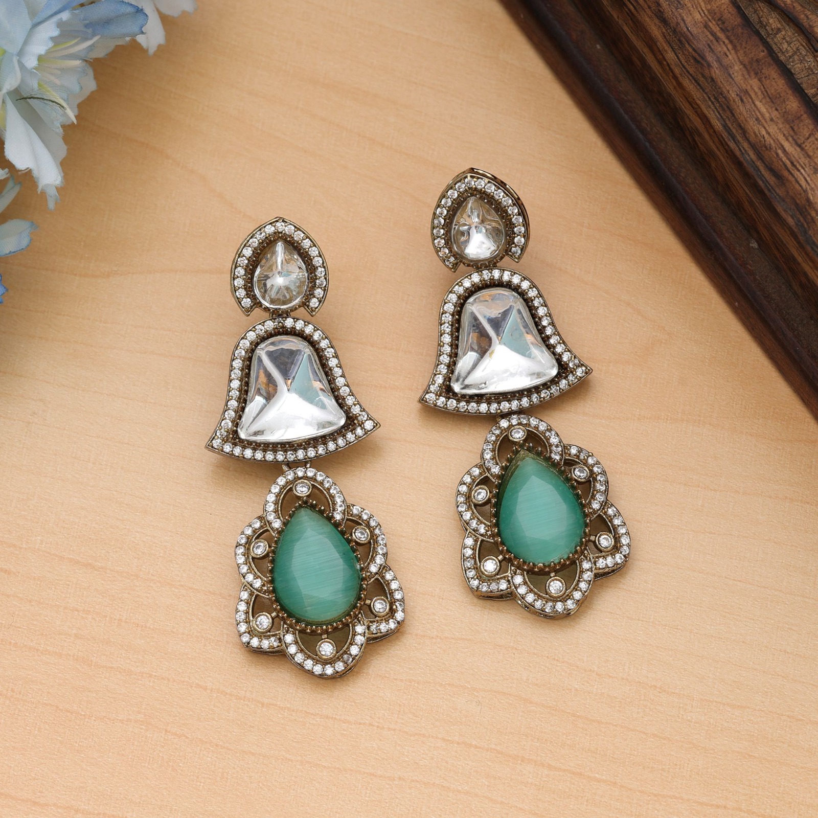 Statement drop earrings featuring bell-shaped clear accents, deep sapphire-blue Monalisa stone teardrop pendants, and a micro-pave American Diamond halo.