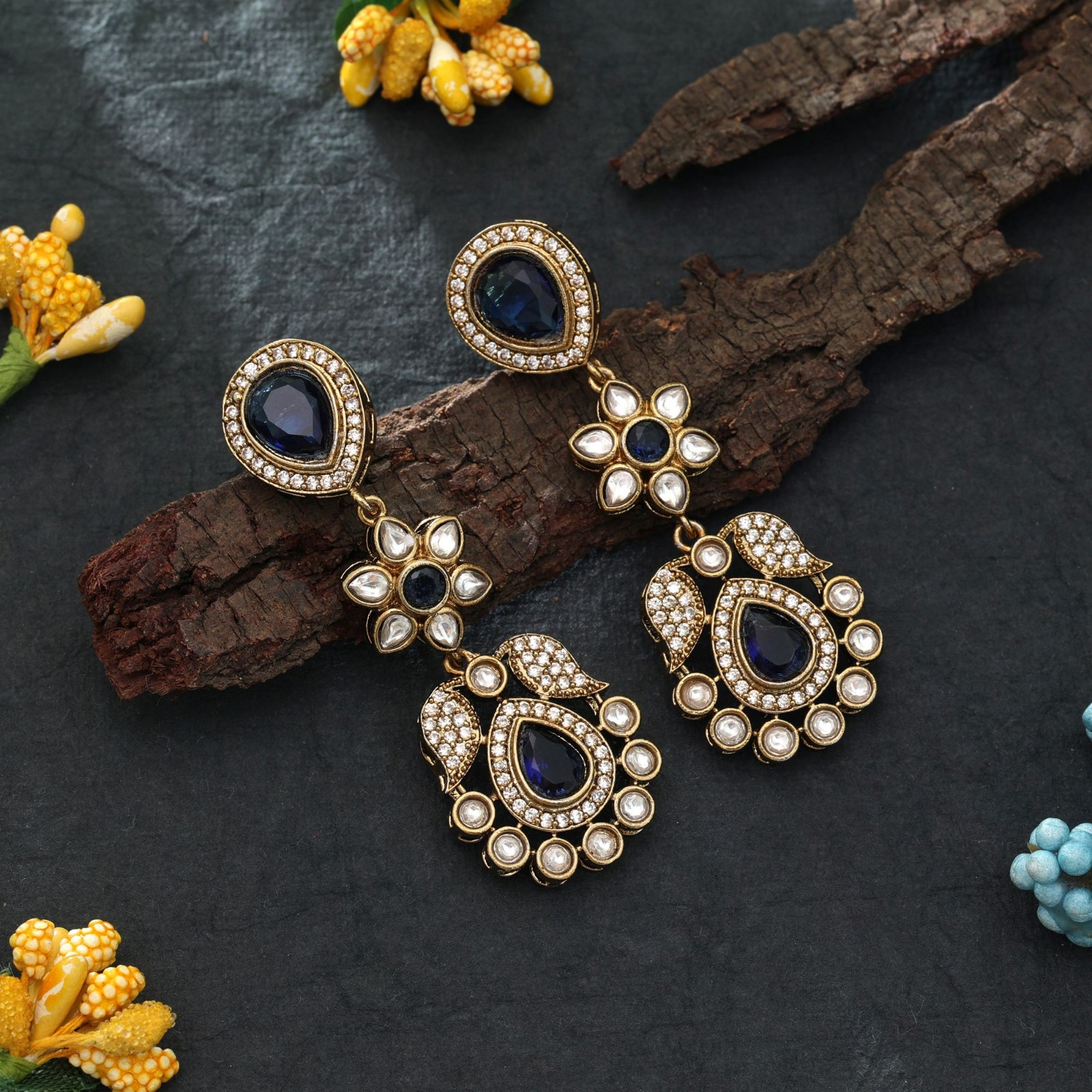 Pair of antique gold drop earrings with teardrop royal blue Monalisa stones, floral Kundan motifs, and sparkling American Diamond micro-pave borders.