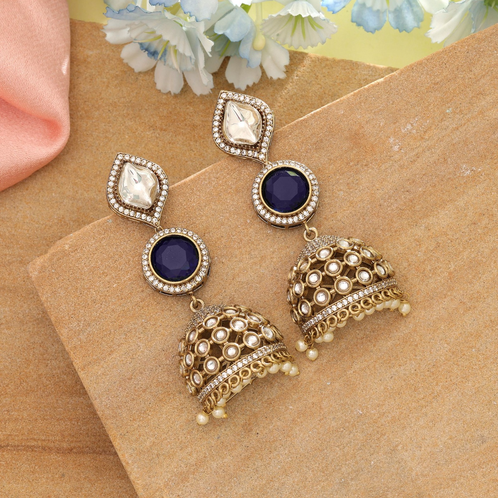 Antique gold statement jhumka earrings featuring leaf-shaped Kundan studs, circular royal blue Monalisa stones, and pearl-beaded dome drop pendants.