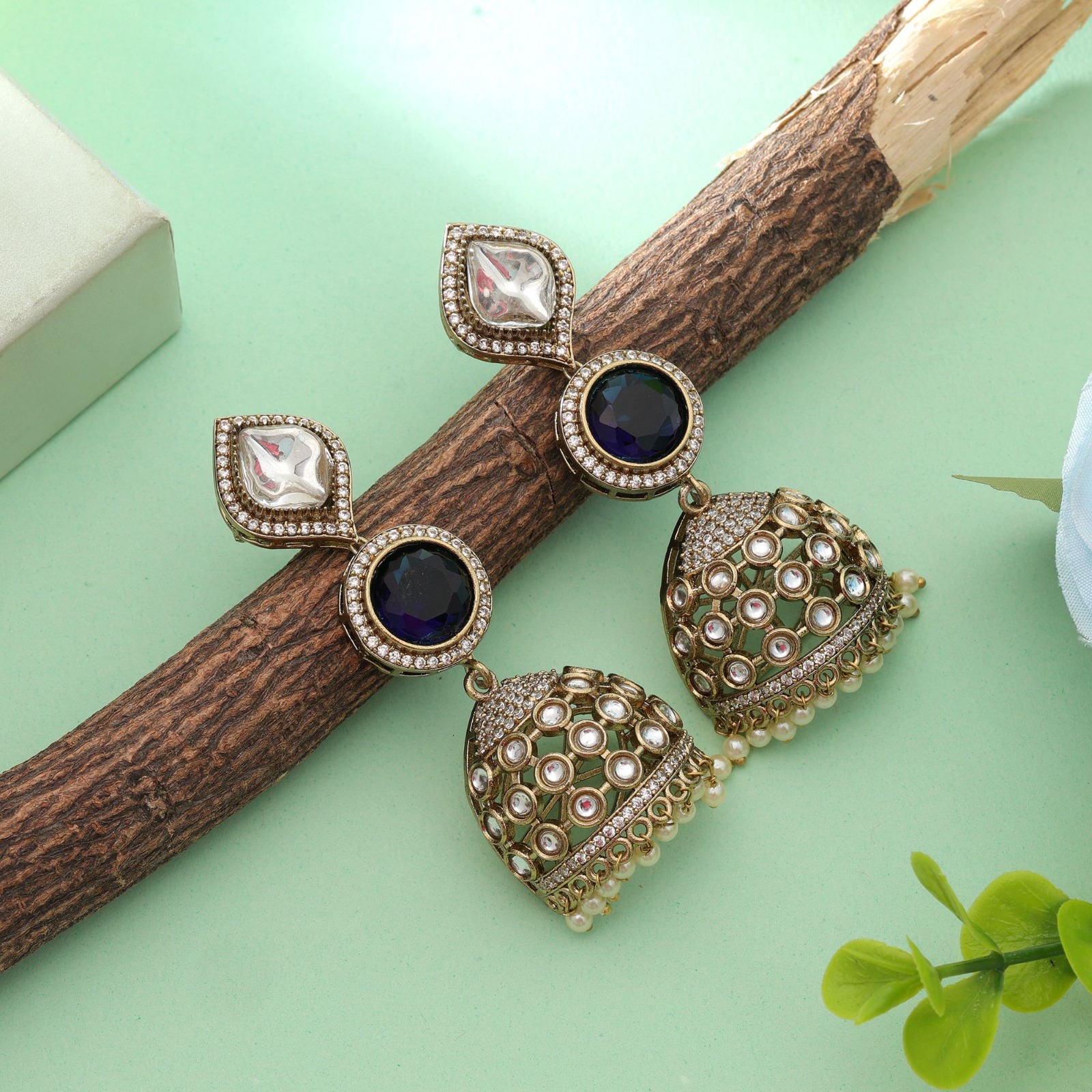 Antique gold statement jhumka earrings featuring leaf-shaped Kundan studs, circular royal blue Monalisa stones, and pearl-beaded dome drop pendants.