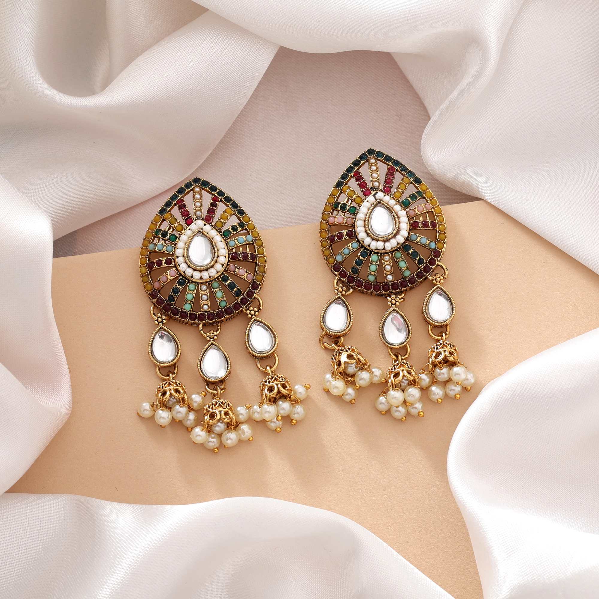 A pair of traditional gold-plated multi-color Navratna-inspired statement earrings, featuring a teardrop-shaped top piece filled with segmented colorful rhinestones surrounding a central white stone, and three dangling teardrop elements finished with delicate clusters of white faux pearls.