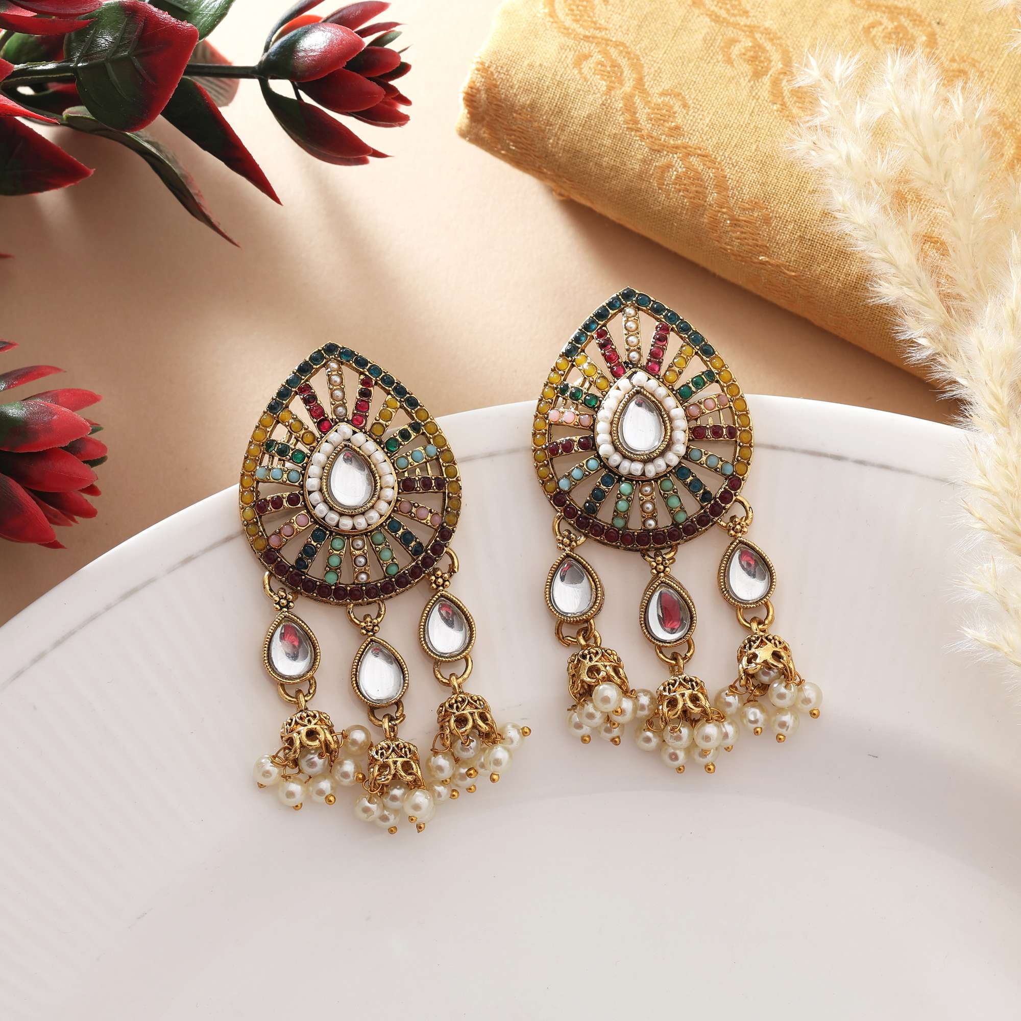 A pair of traditional gold-plated multi-color Navratna-inspired statement earrings, featuring a teardrop-shaped top piece filled with segmented colorful rhinestones surrounding a central white stone, and three dangling teardrop elements finished with delicate clusters of white faux pearls.